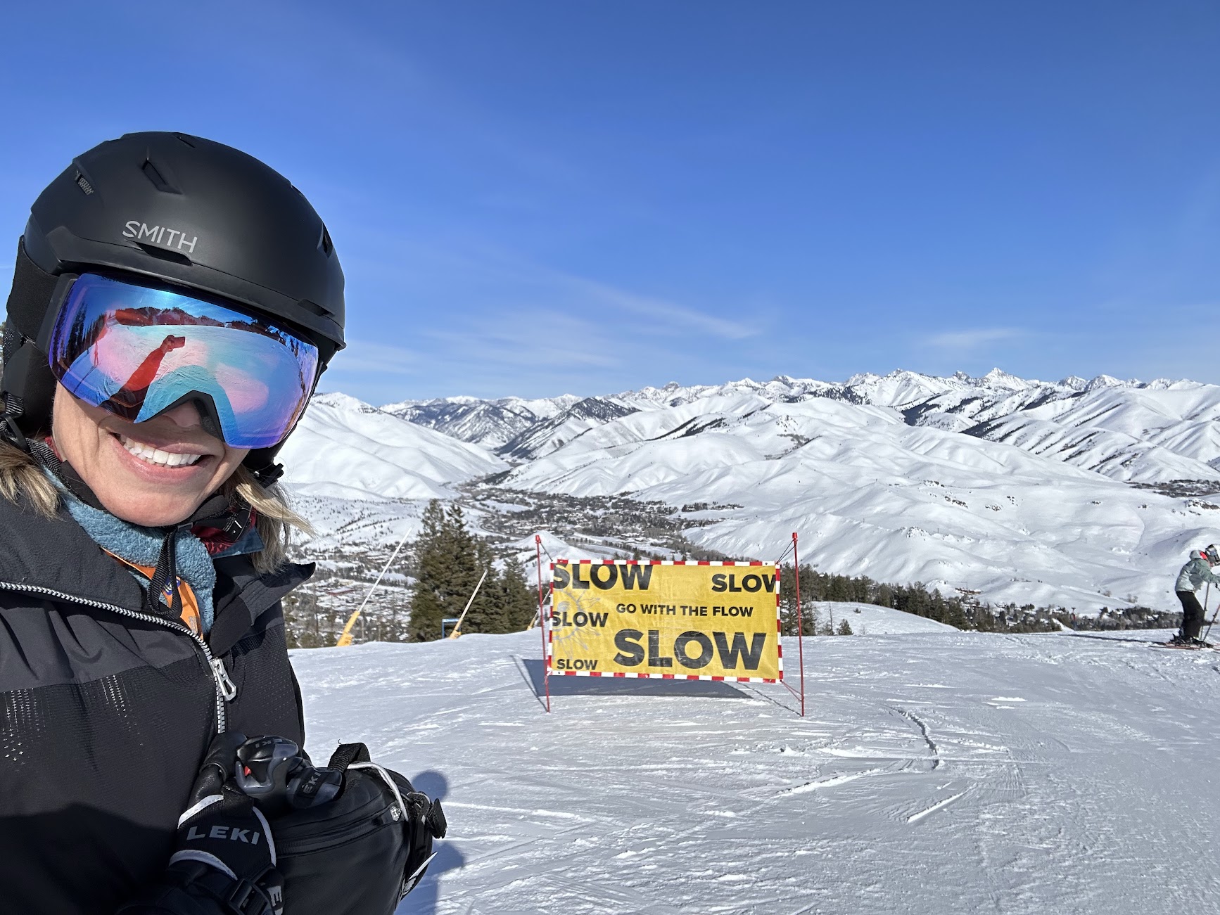 Mary Christianson enjoying some work-life balance on the slopes — standing in ski gear next to a yellow sign that says, "Slow. Go with the flow."